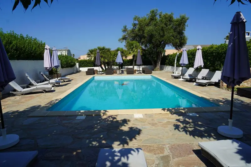 Une piscine rectangulaire entourée de transats et de parasols sous un ciel bleu.