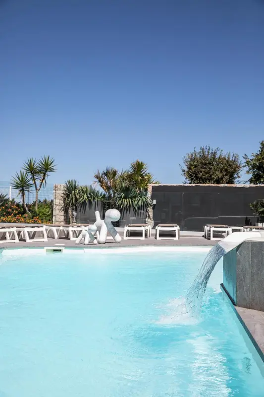 Une piscine bleue avec une cascade et des chaises longues blanches.