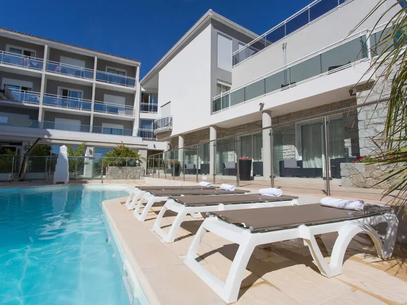 Transats alignés au bord d'une piscine ensoleillée devant un bâtiment moderne.