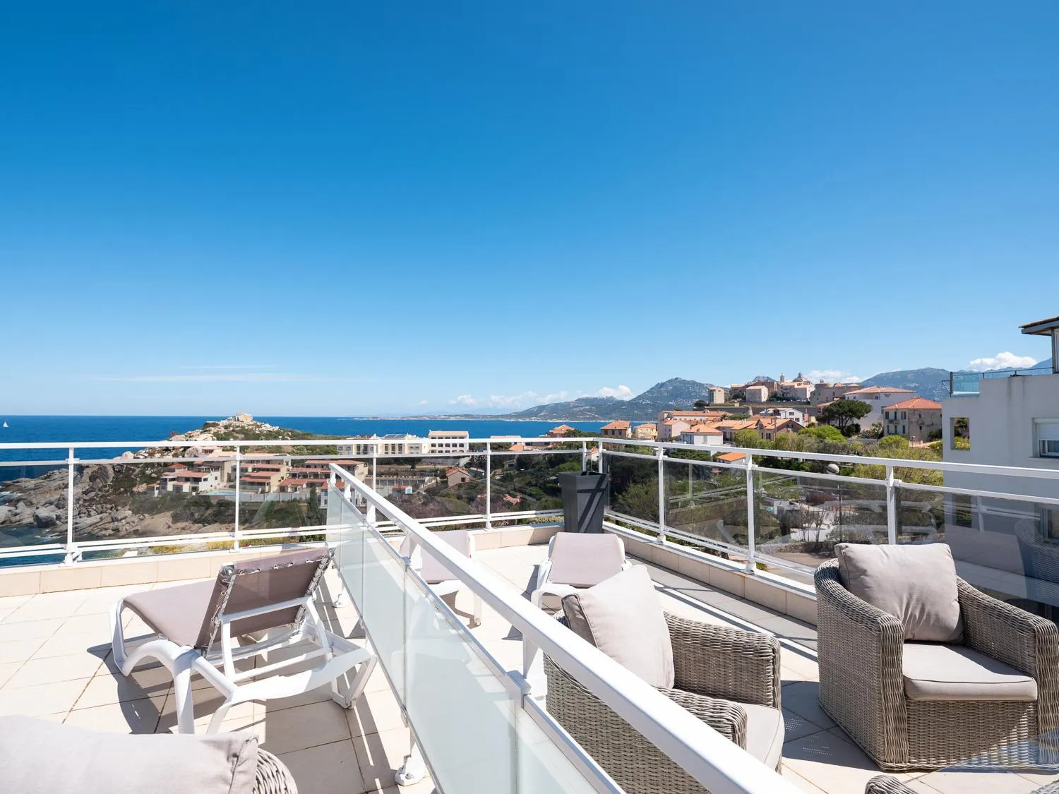 Terrasse aménagée avec transats et mobilier de jardin offrant une vue sur la mer et les collines.