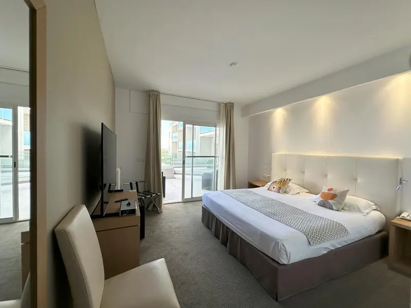Chambre lumineuse avec un grand lit et un accès à une terrasse.