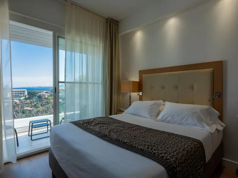 Une chambre lumineuse avec un grand lit et un balcon offrant une vue sur la mer.