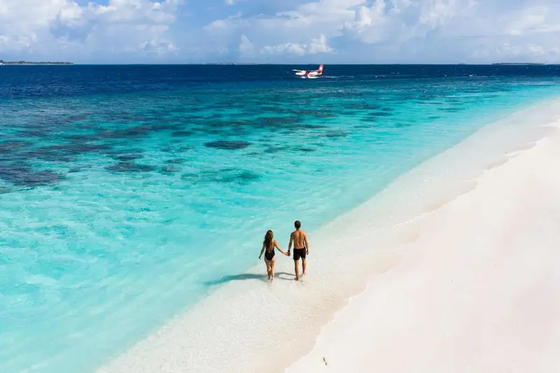 Un couple marche sur une plage de sable blanc bordée d'eau turquoise.