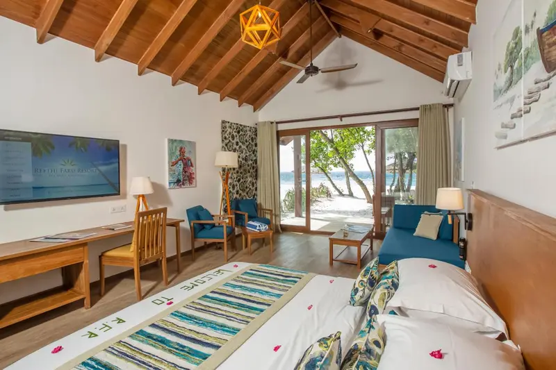 Une chambre lumineuse avec un lit, un bureau et un canapé, donnant sur une plage.