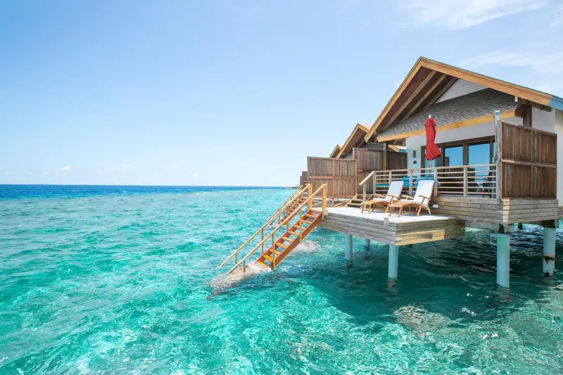 Maisons sur pilotis avec terrasses donnant sur une eau turquoise.