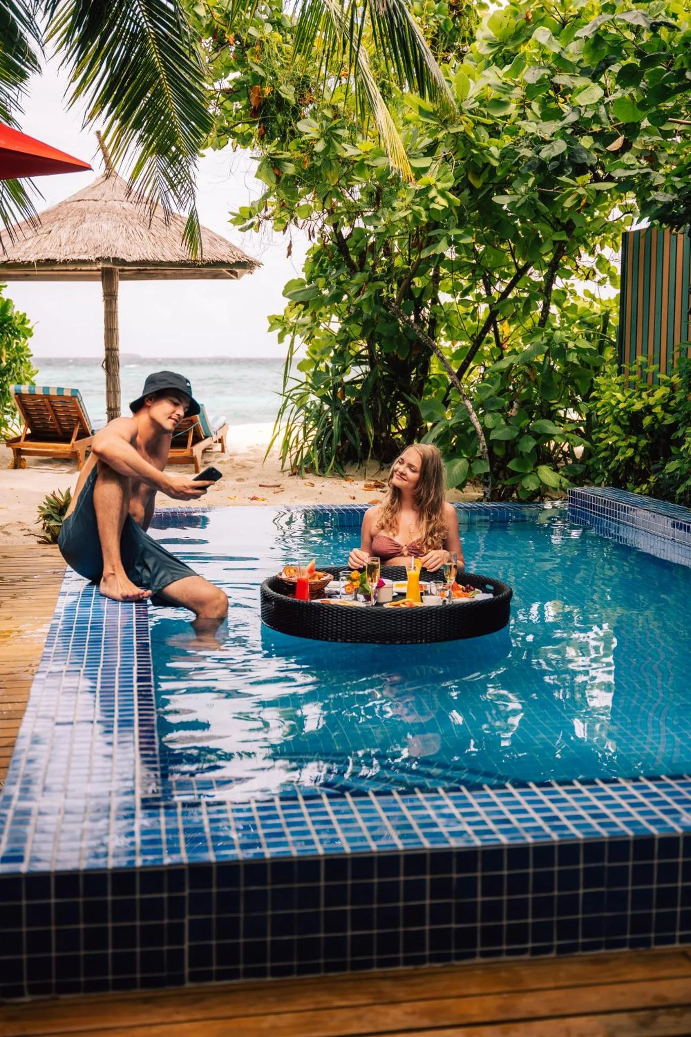 Un couple se détend au bord d'une piscine avec des boissons et des collations.