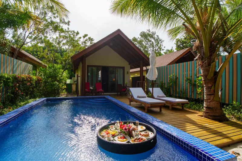 Petits déjeuners flottants servis dans une piscine privée devant des bungalows.