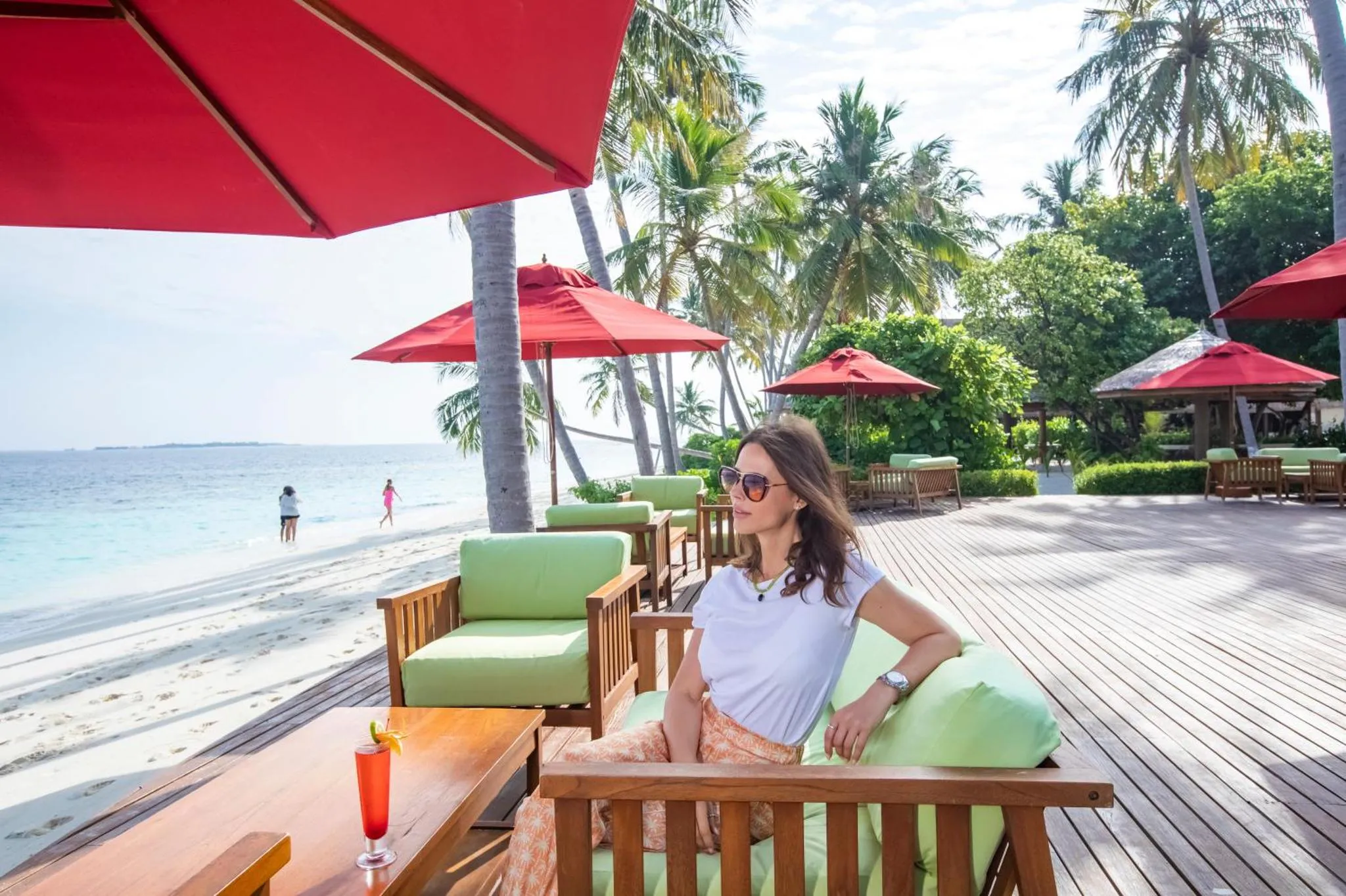Une femme se détend sur une terrasse en bois face à une plage de sable blanc.