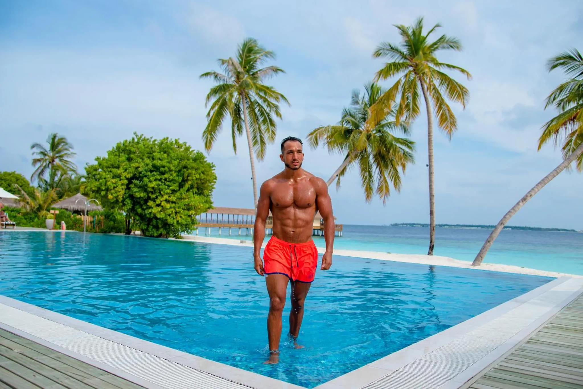 Un homme se tient au bord d'une piscine turquoise face à la mer.