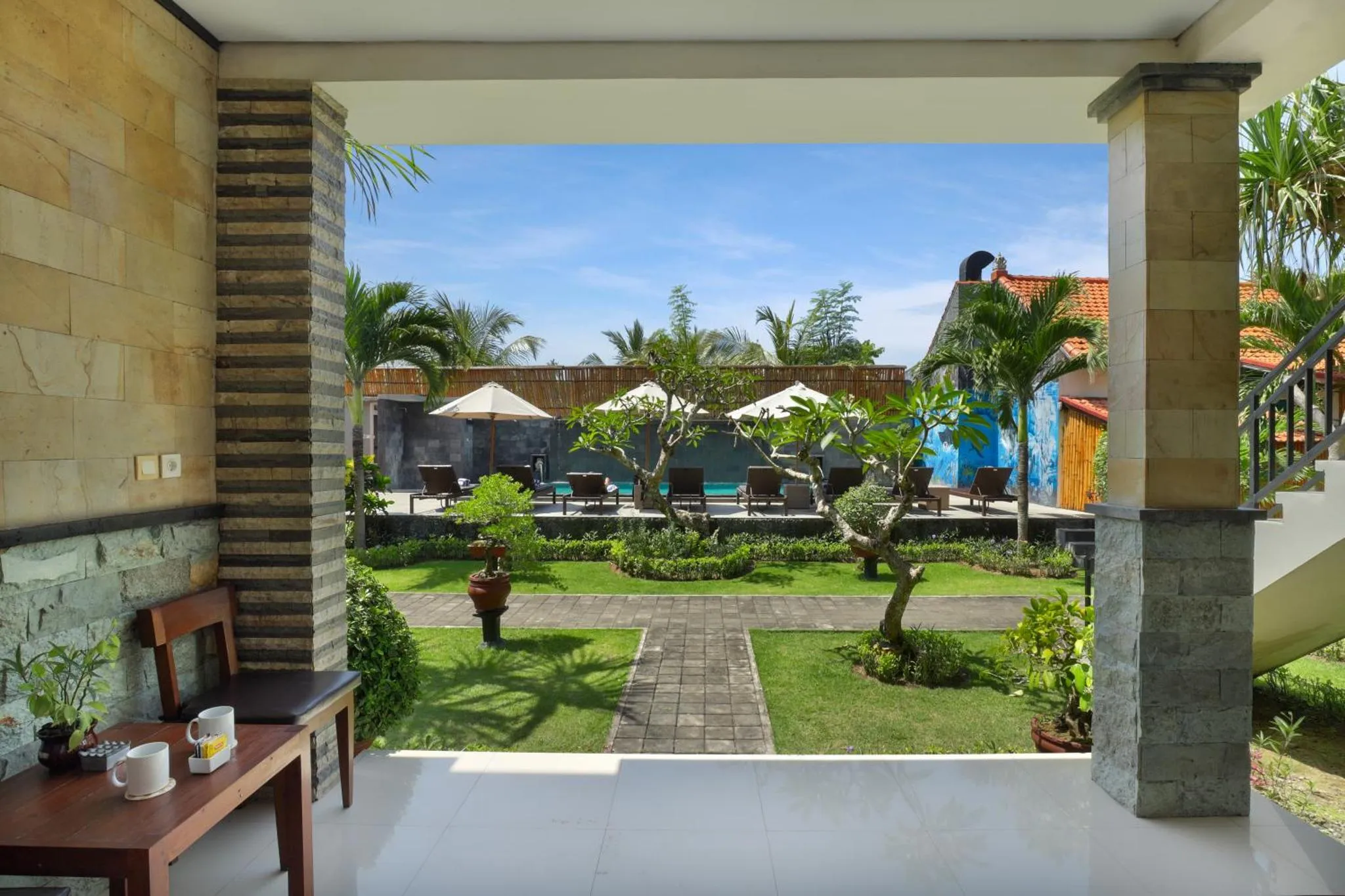 Vue sur une piscine et un jardin depuis une terrasse ombragée.