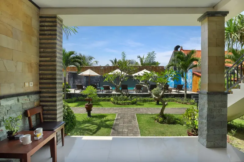 Vue sur une piscine et un jardin depuis une terrasse ombragée.