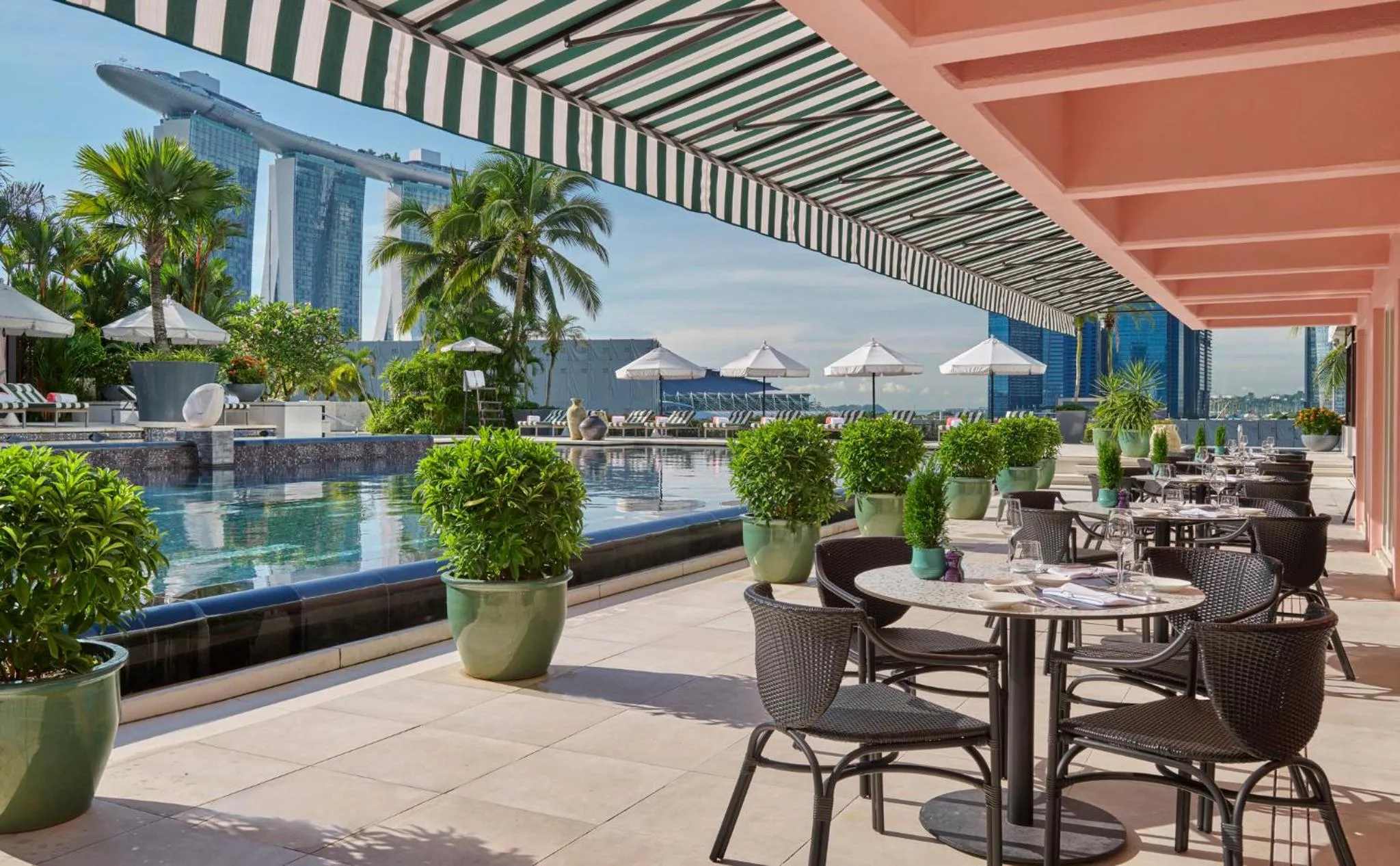 Terrasse ombragée avec tables et chaises près d'une piscine.