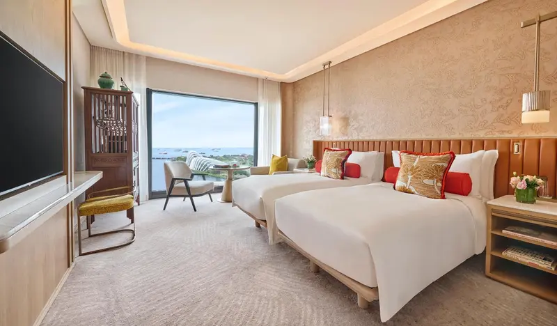 Chambre lumineuse avec deux lits simples et vue sur la mer.