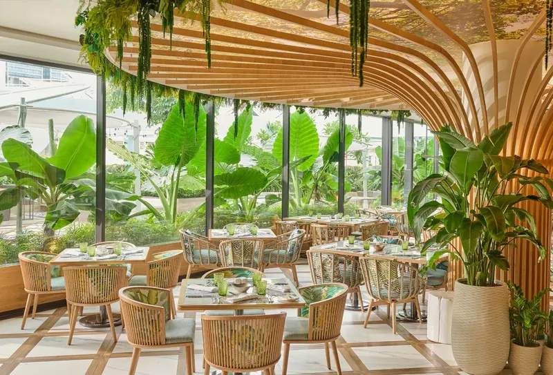 Une salle lumineuse avec des tables et des chaises en osier, donnant sur une végétation luxuriante.
