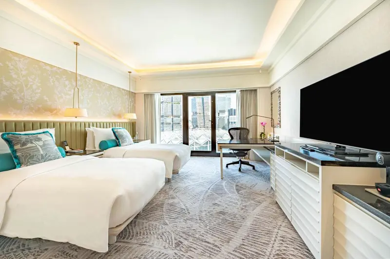 Chambre lumineuse avec deux lits et un bureau près d'une fenêtre.