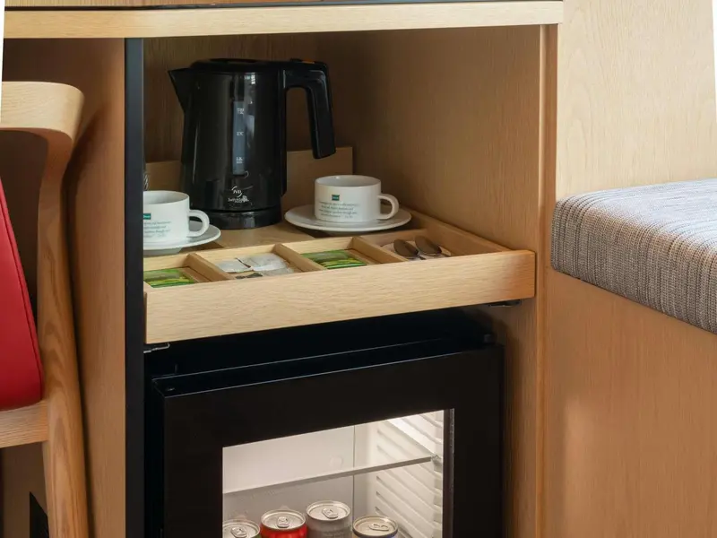 Une bouilloire électrique et une tasse sur un plateau en bois, devant un réfrigérateur.