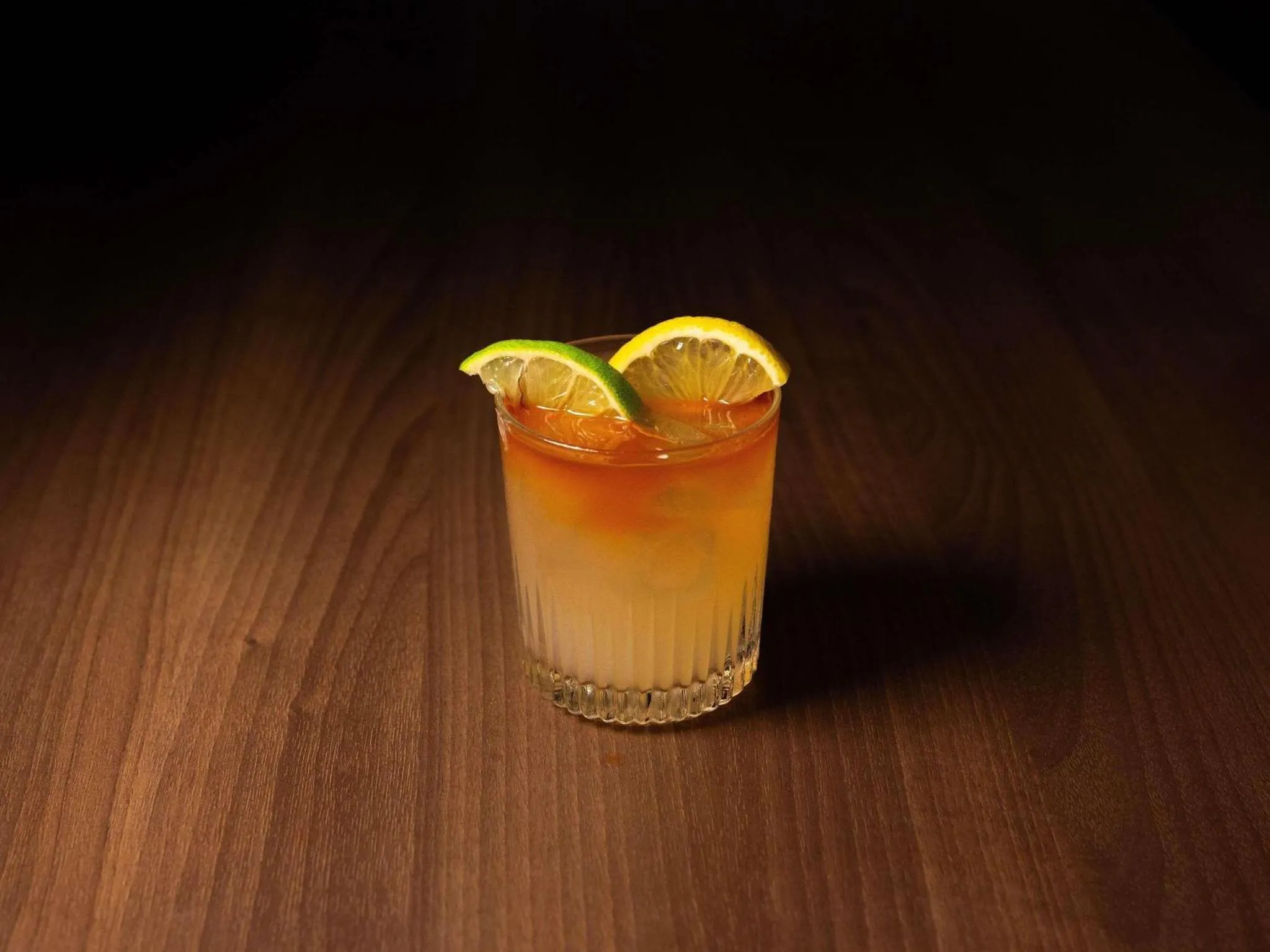 Un verre de cocktail aux agrumes est présenté sur une surface en bois sombre.