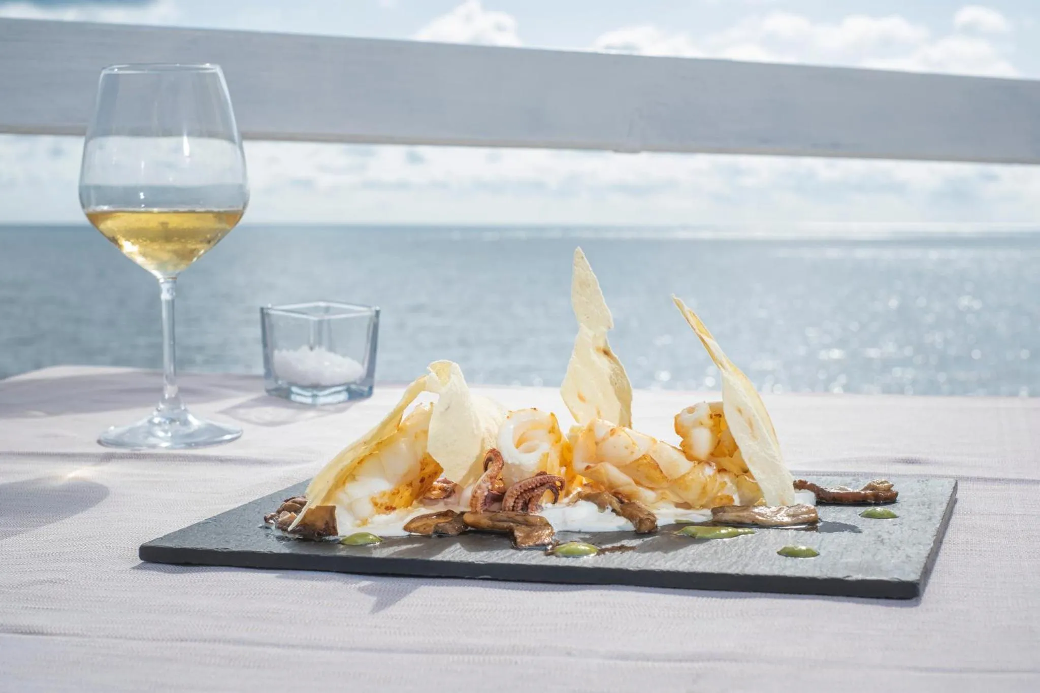 Assiette de fruits de mer et verre de vin sur une table en extérieur avec vue sur la mer.