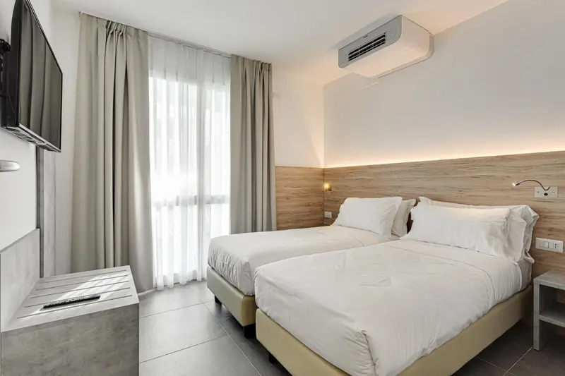 Une chambre lumineuse avec deux lits simples et un téléviseur mural.