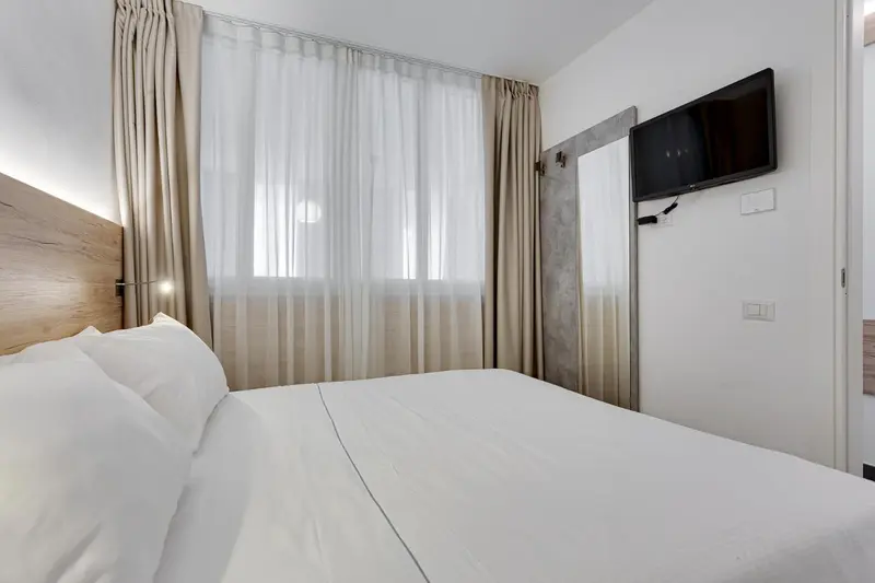 Une chambre lumineuse avec un grand lit recouvert de draps blancs et une télévision murale.