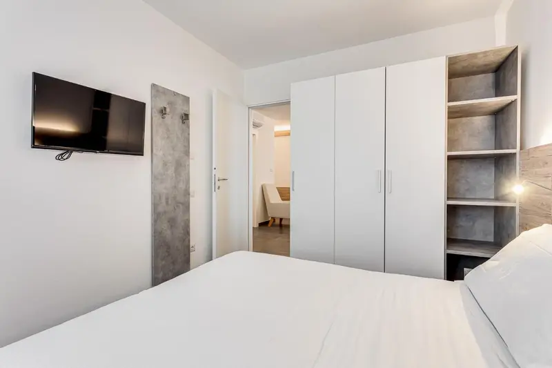 Une chambre lumineuse avec un lit blanc et un meuble de rangement.