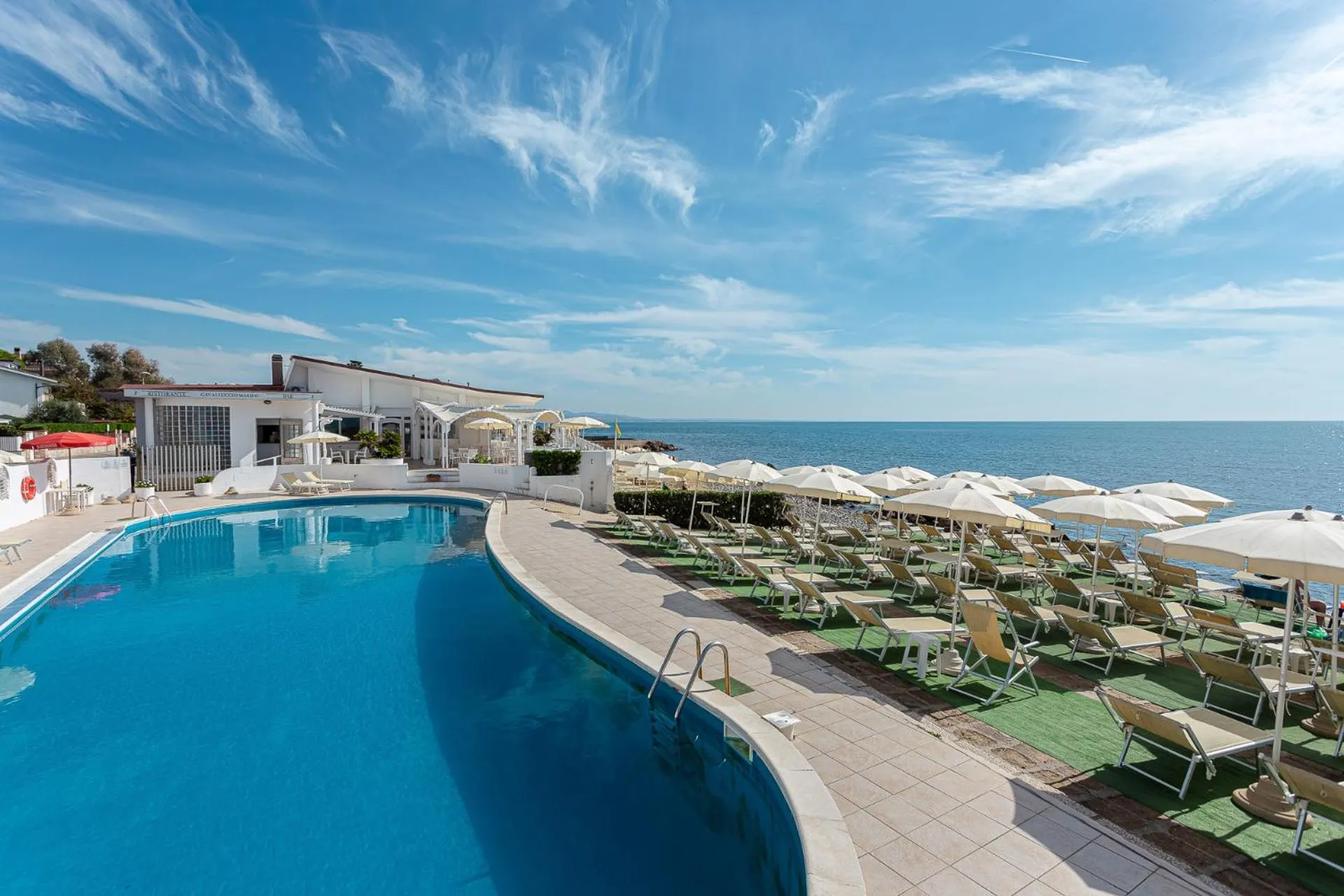 Piscine bleue bordée de transats sous des parasols, avec vue sur la mer.