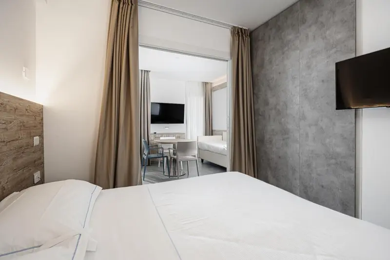 Une chambre avec un lit fait et un espace salon visible au fond.