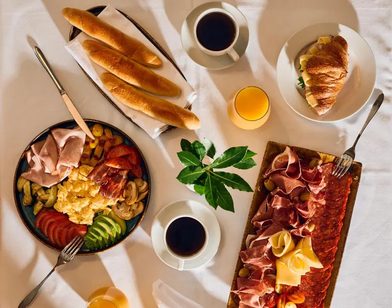 Table dressée avec un petit-déjeuner copieux composé de viennoiseries, de charcuterie, d'œufs et de boissons.