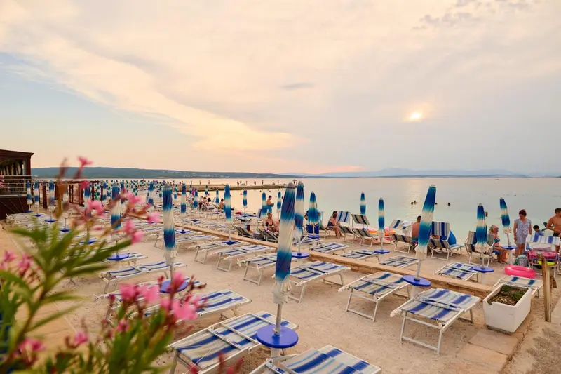 Transats bleus et parasols sur une plage de sable au coucher du soleil.