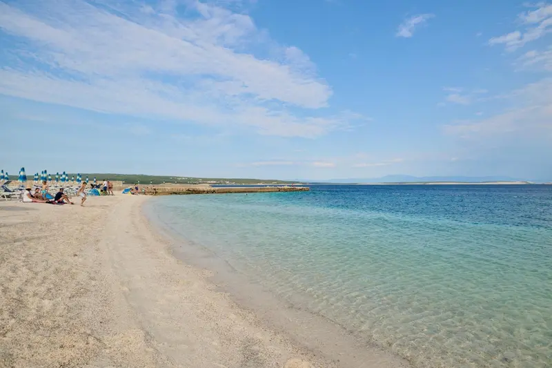 Plage de sable fin bordée d'une mer turquoise sous un ciel bleu nuageux.