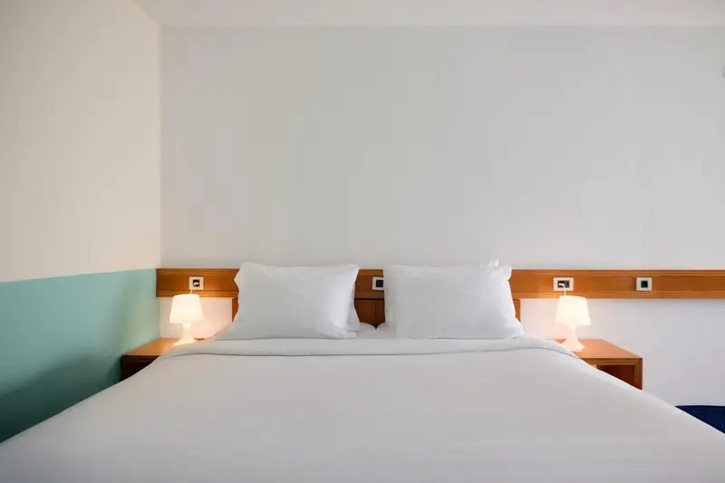 Lit double avec oreillers blancs dans une chambre lumineuse.