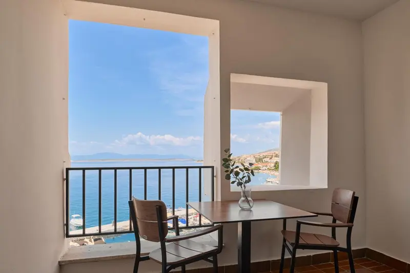 Une table et des chaises sont placées devant une fenêtre donnant sur la mer.