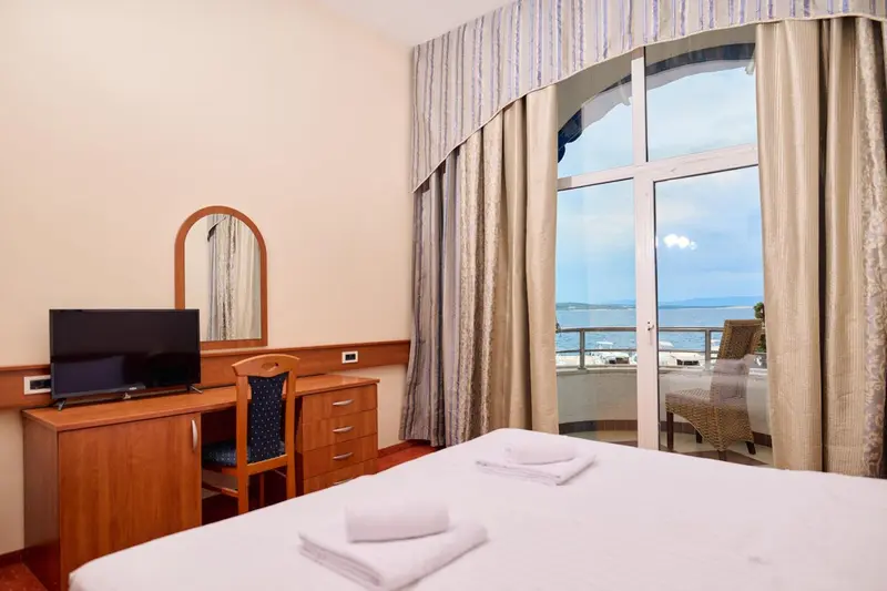 Chambre lumineuse avec vue sur la mer depuis un balcon.