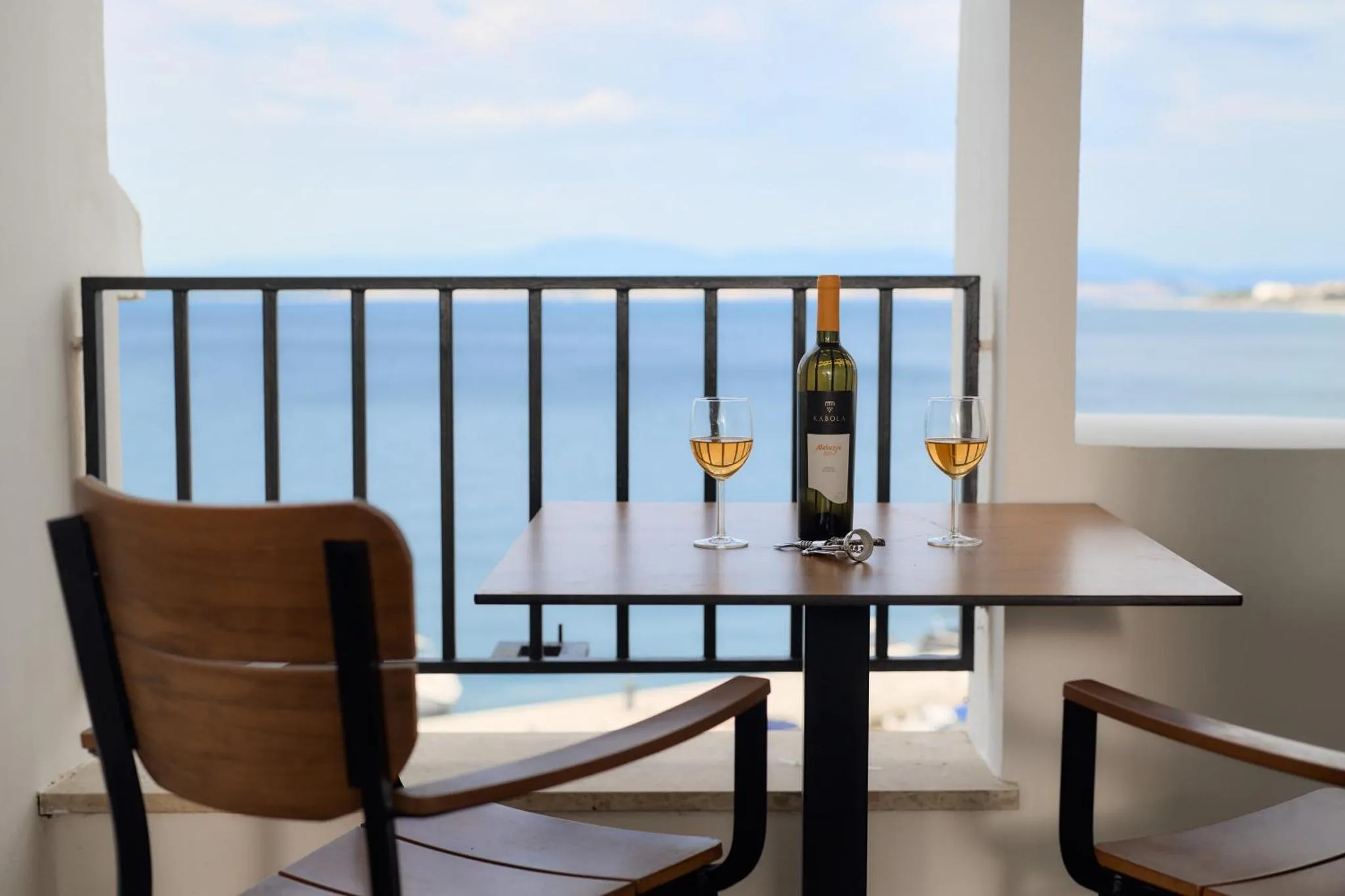 Une table avec deux verres de vin et une bouteille sur un balcon avec vue sur la mer.