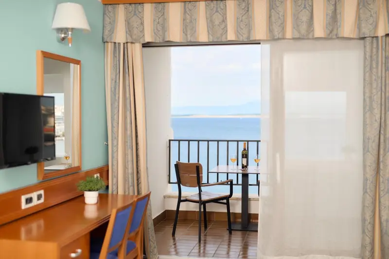 Une chambre lumineuse s'ouvre sur une vue mer et un balcon avec table.