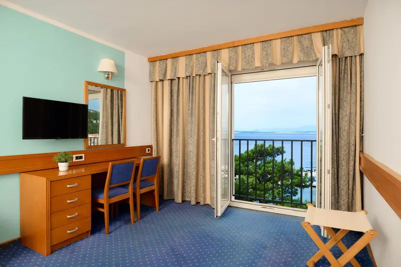 Une chambre lumineuse avec un bureau et un balcon donnant sur la mer.