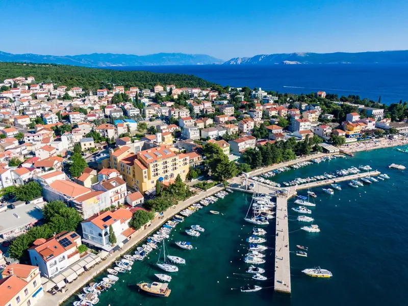 Vue aérienne d'une ville côtière avec un port de plaisance et des bâtiments aux toits rouges.