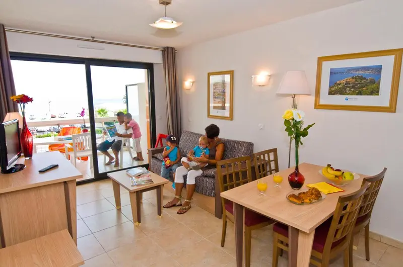 Une famille se détend dans un salon lumineux avec accès à un balcon.