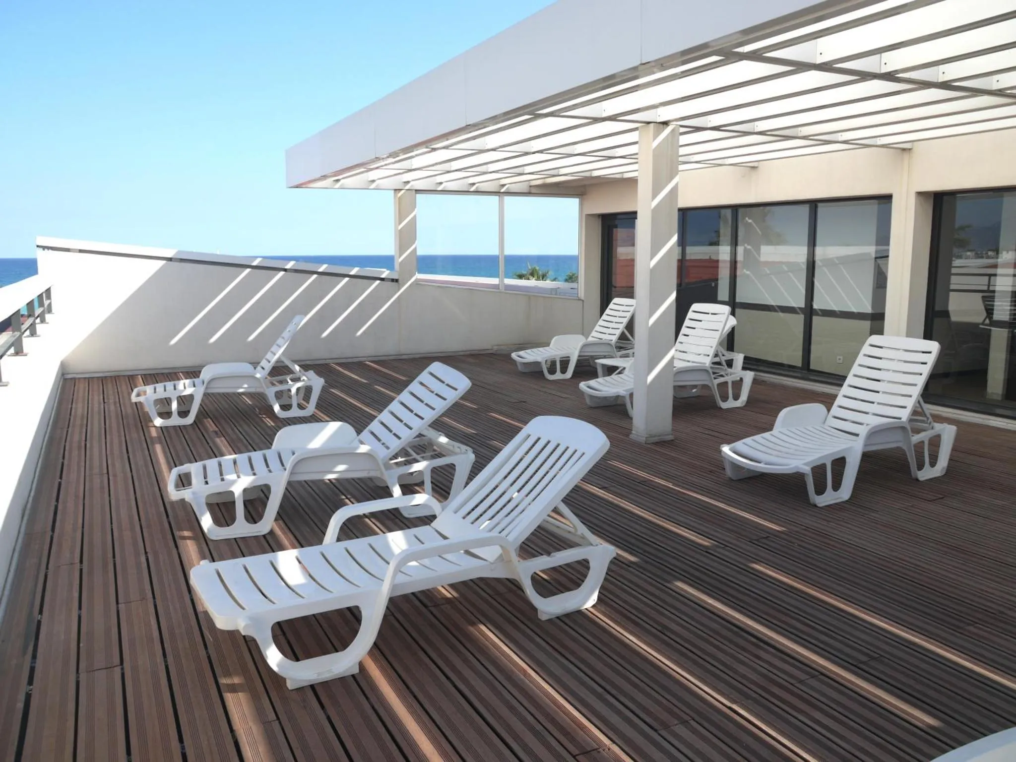 Terrasse en bois avec transats blancs sous une structure ombragée.