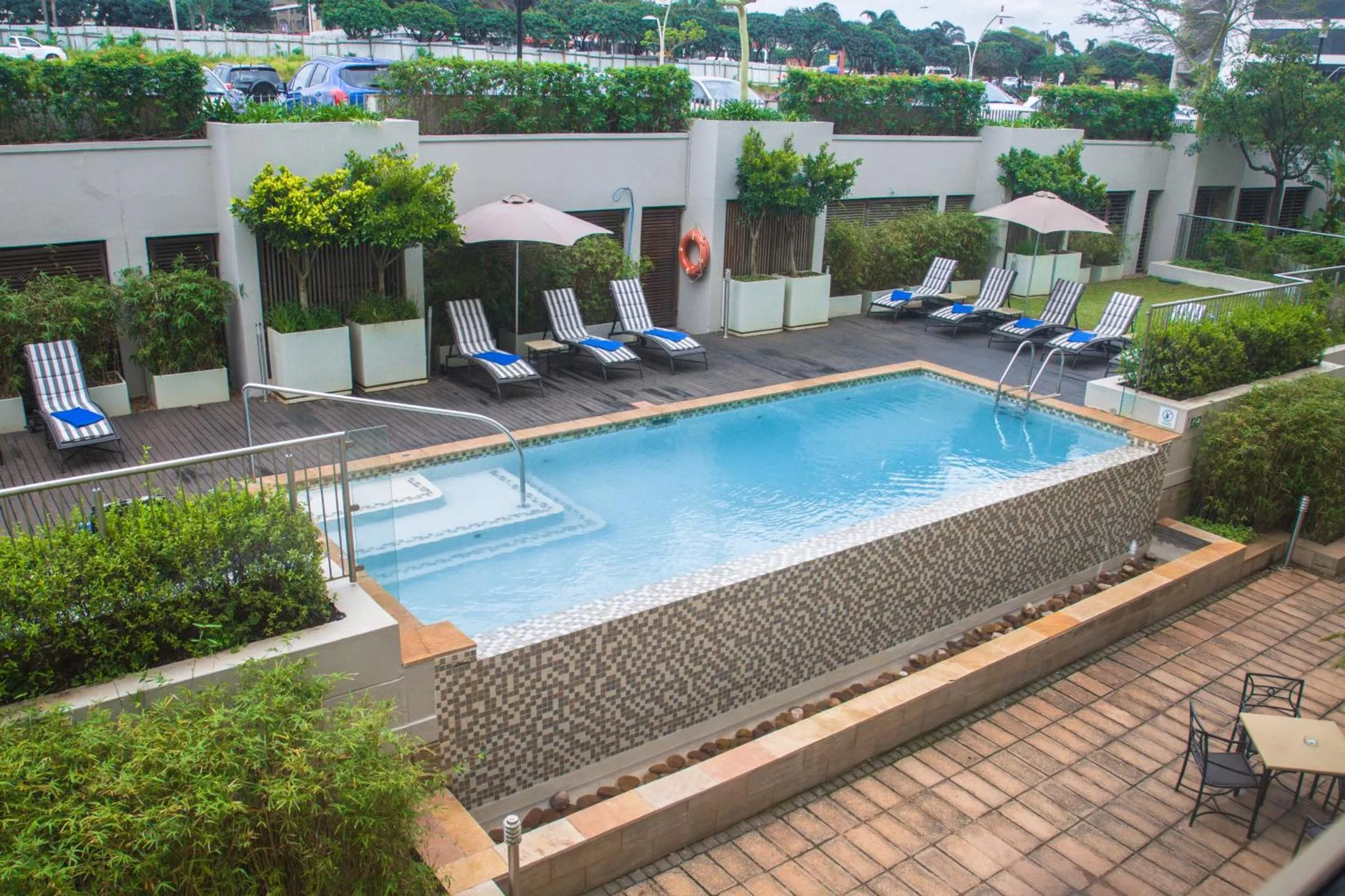 Piscine rectangulaire entourée d'un sol en mosaïque et de chaises longues.