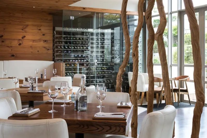Une salle à manger lumineuse avec des tables dressées et une cave à vin visible.