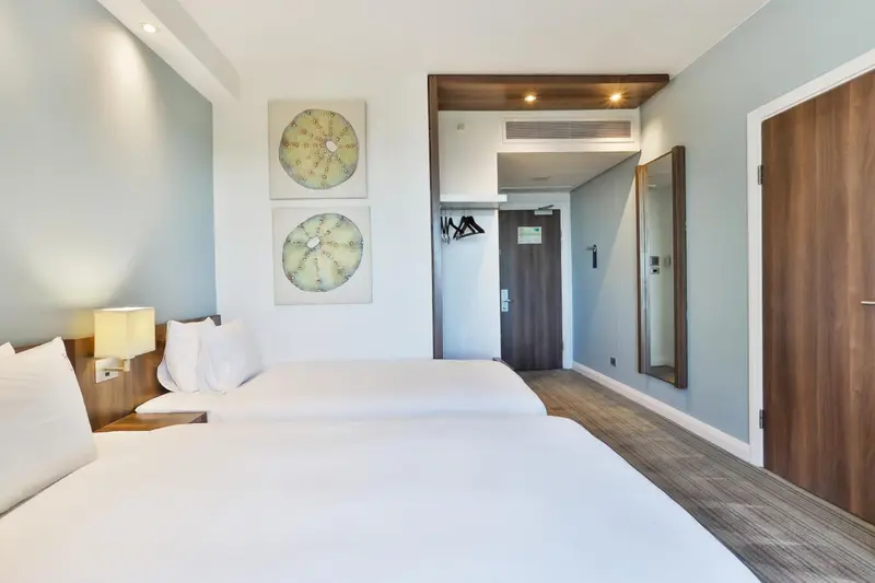 Une chambre lumineuse avec deux lits simples et un décor mural abstrait.
