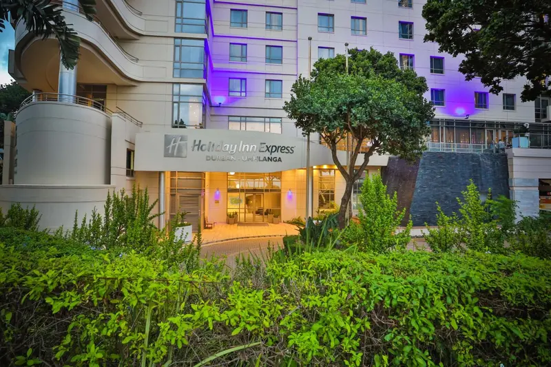 Façade d'un bâtiment moderne avec végétation tropicale et entrée illuminée.