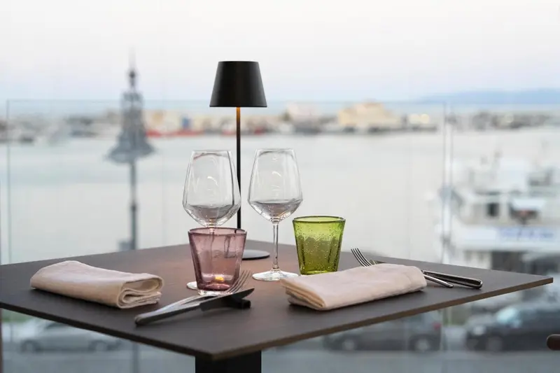 Une table dressée avec des verres et des couverts face à une vue sur le port.