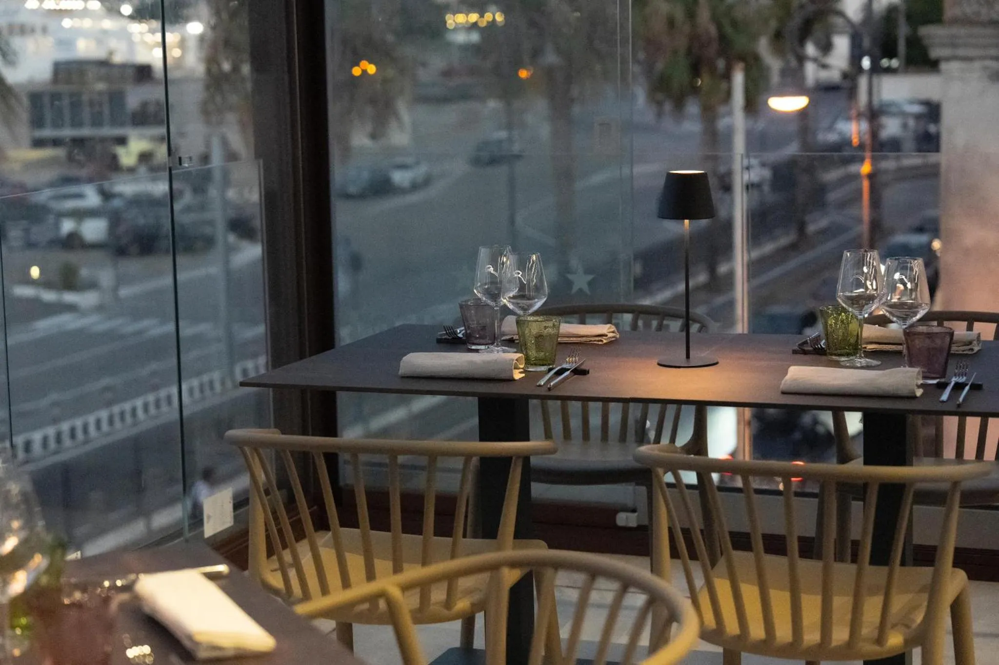 Une table est dressée devant une grande baie vitrée donnant sur une rue illuminée.