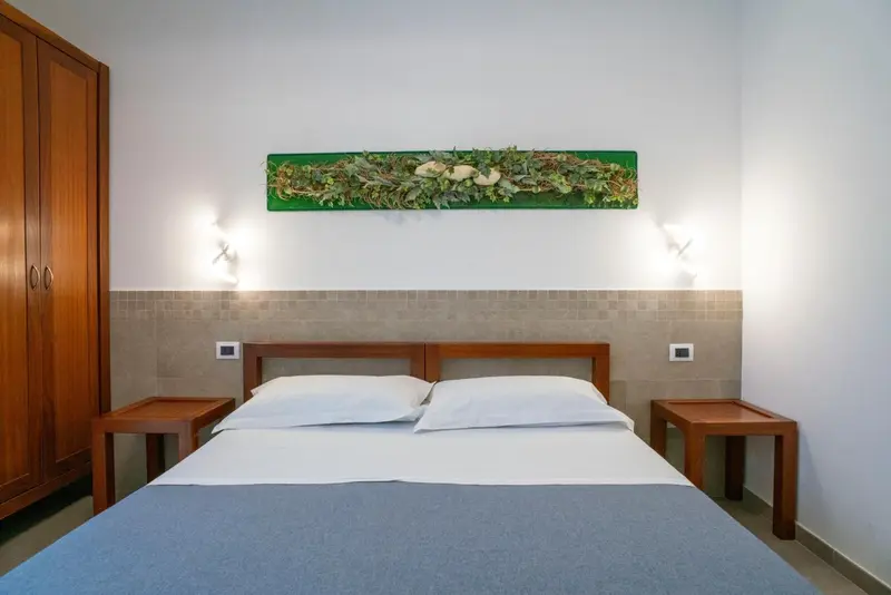 Une chambre lumineuse avec un grand lit et une décoration murale végétale.