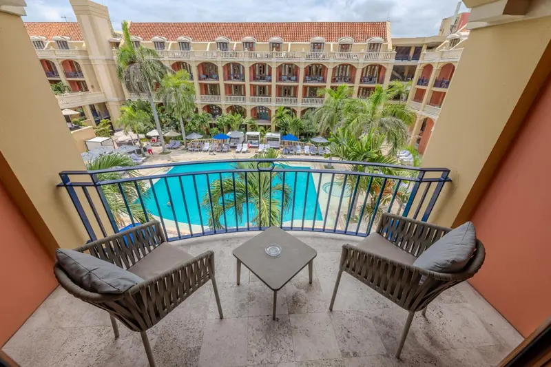 Vue d'un balcon avec mobilier donnant sur une piscine et un jardin tropical.