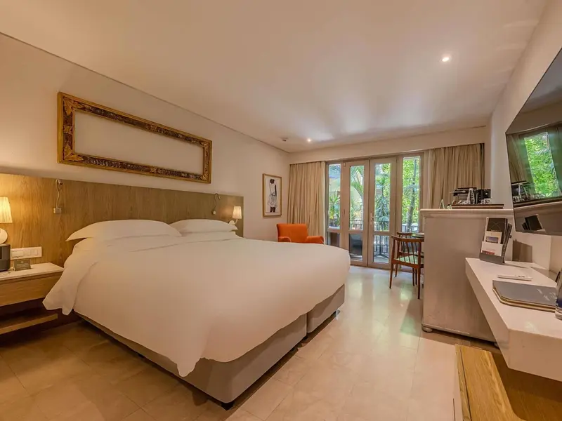 Une chambre lumineuse avec un grand lit et un fauteuil près d'une baie vitrée.