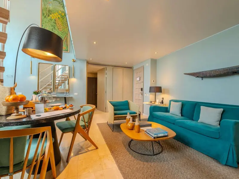 Un salon lumineux avec un coin repas et un canapé turquoise.