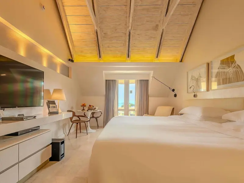 Une chambre lumineuse avec un lit blanc et un bureau.